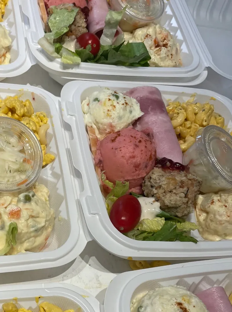Takeout containers filled with salad, macaroni, potato salad and sliced ham